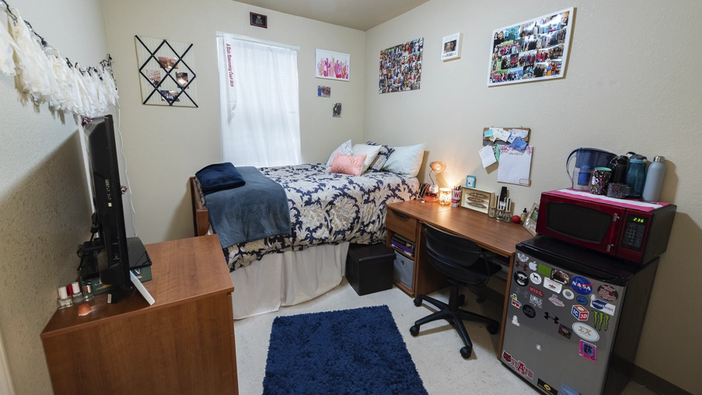 Bedroom with floral bedding, wooden dresser with TV, desk with chair, and decorative wall art.