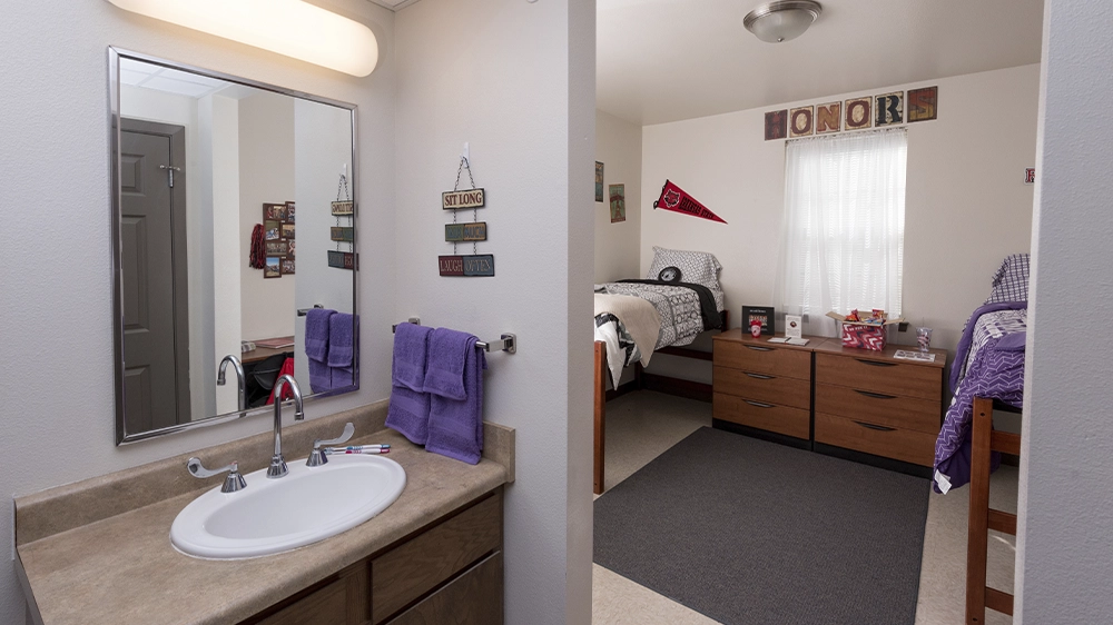 View from bathroom into shared bedroom with two twin beds and wooden dresser.