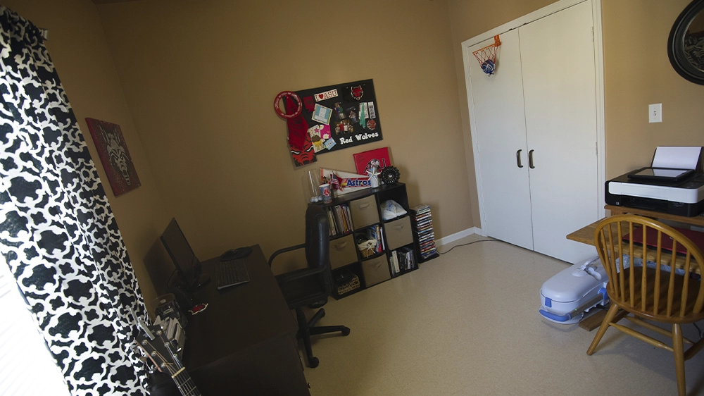 Bedroom with desk, chair, and closet doors, featuring wall decor and shelving.