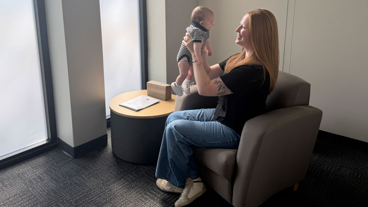 A woman holds a baby in a tan room