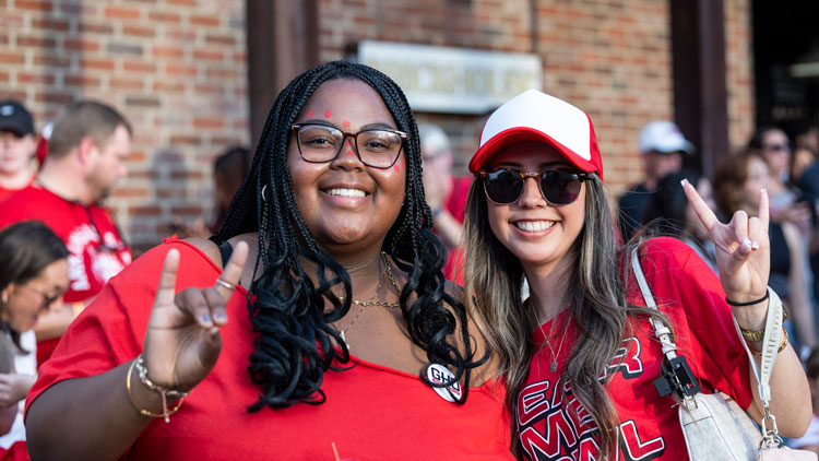 two women wearing red make the "howl" symbol with their hands.