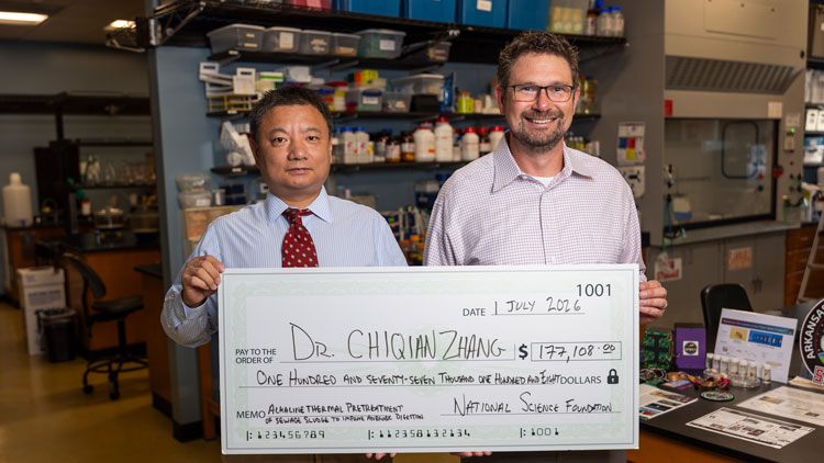 Two people holding a big check in a lab space
