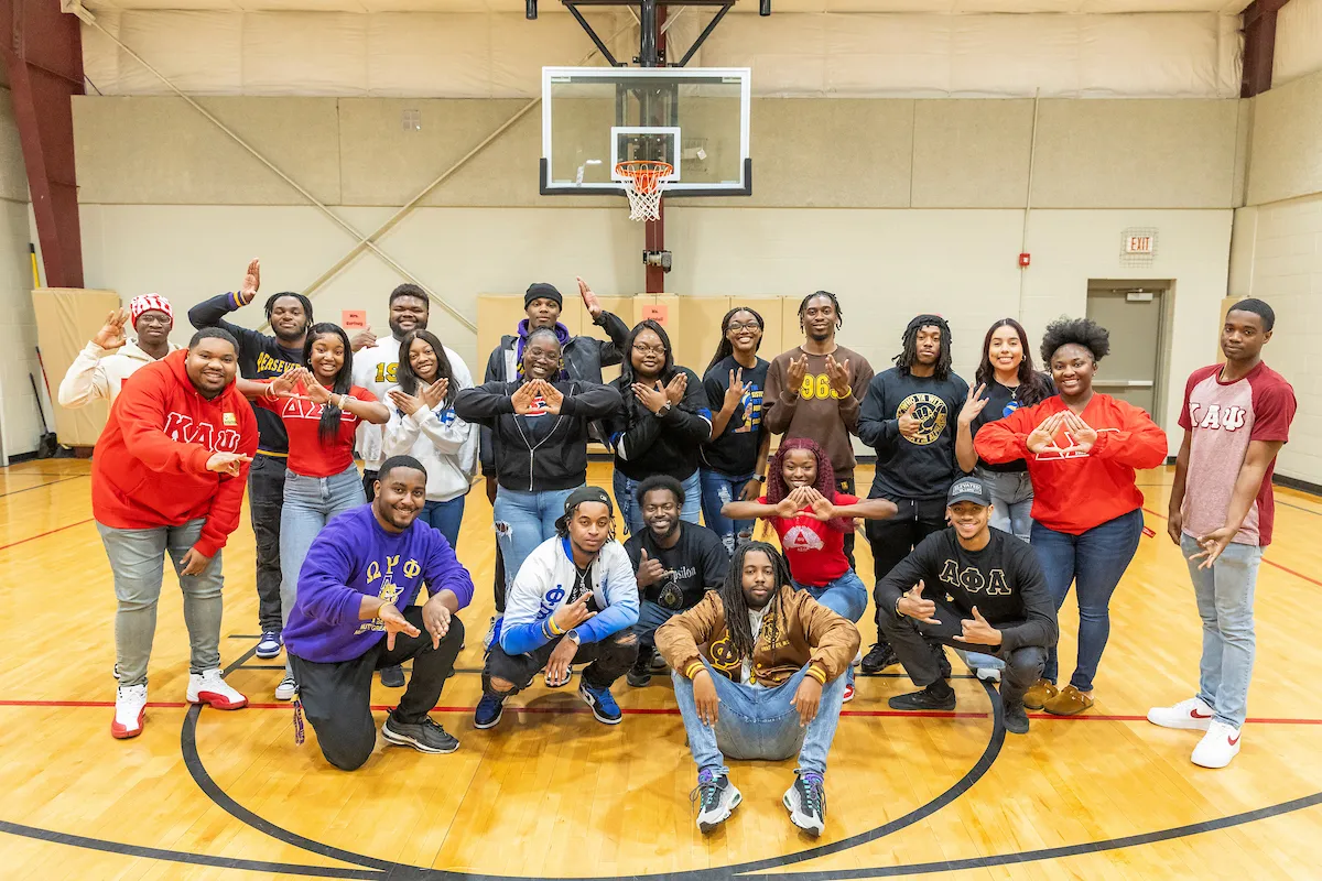 NPHC members pose in gymnasium during community outreach program at a local school.