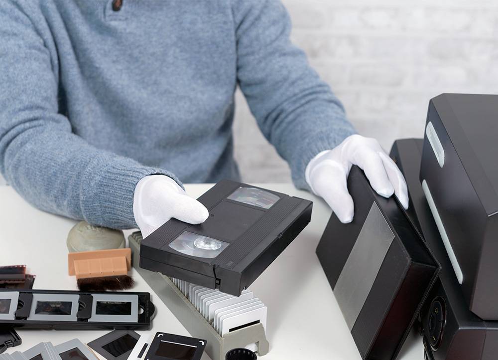 Person holding VHS tape over table with projector slides and other physical media