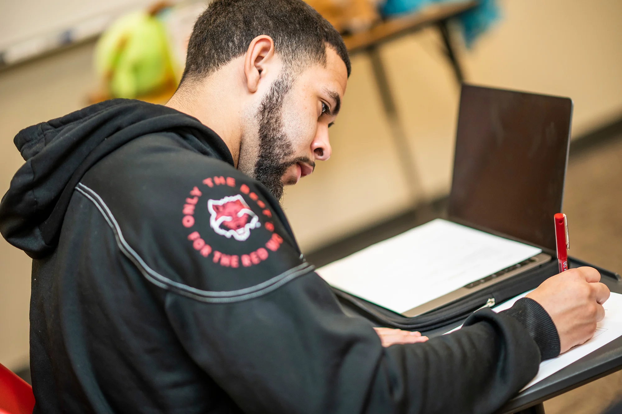 A student wearing a Red Wolves jacket writing on a piece of paper.