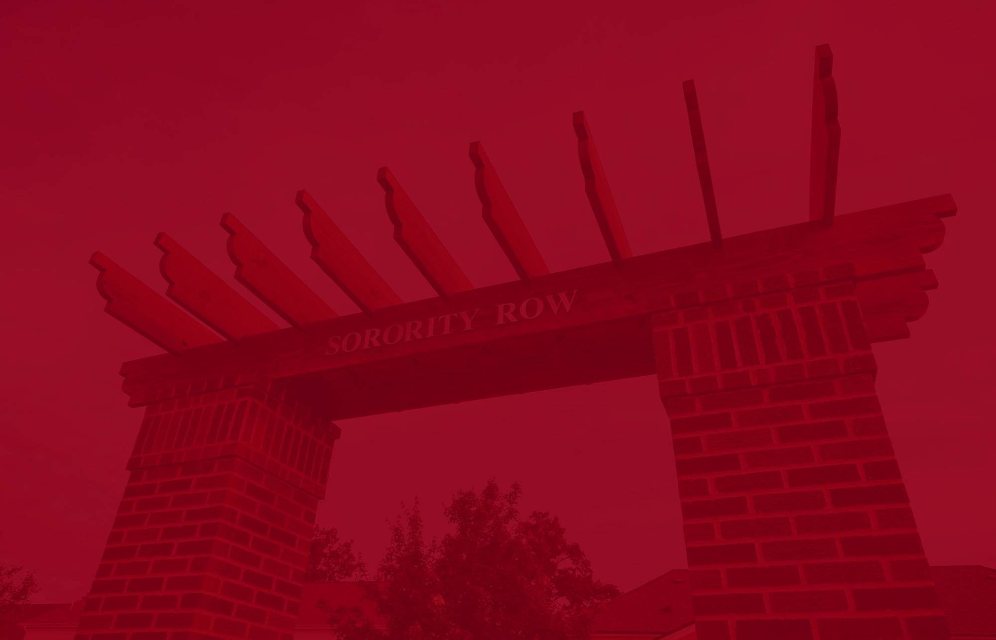 Brick archway with wooden beams forming a pergola-style top, featuring the engraved words “Sorority Row.” The image has a red color overlay, and trees and rooftops are faintly visible in the background.