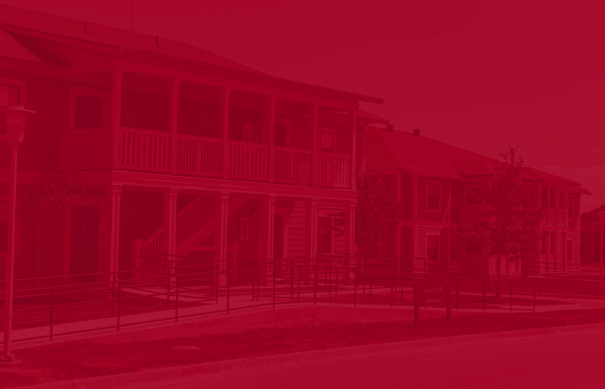Two apartment buildings at The Village with covered balconies and white railings, shown with a solid red color overlay for design effect.
