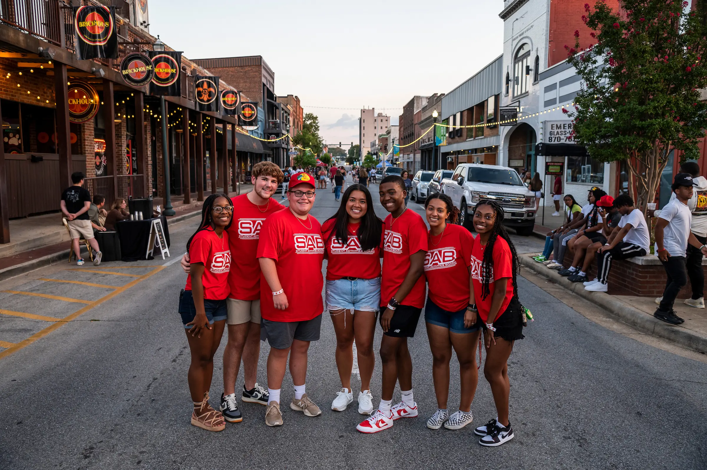 Smiling students in red Student Activities Board (SAB) shirts pose together at a lively outdoor campus or community event.
