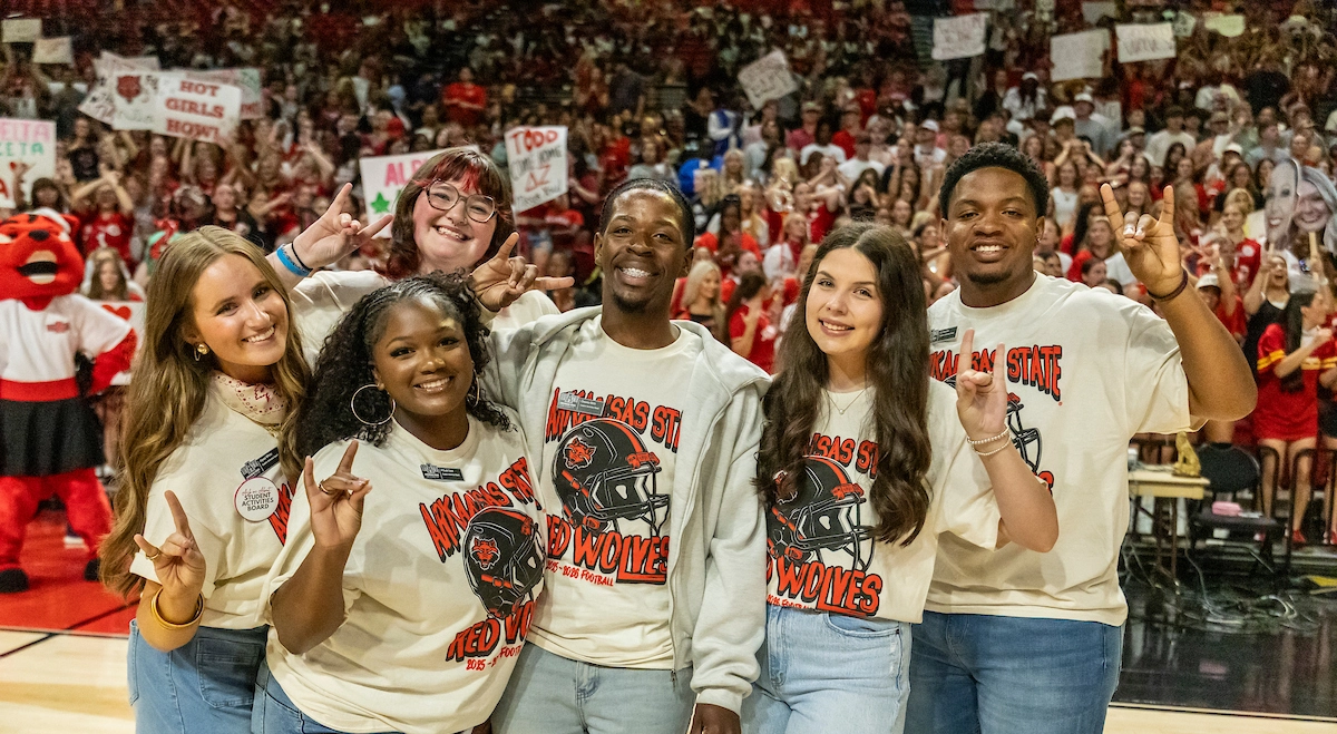 Student Activities Board students with their hands making a 'wolves up' sign in front of a crowd of students at the Order of the Pack pep rally.