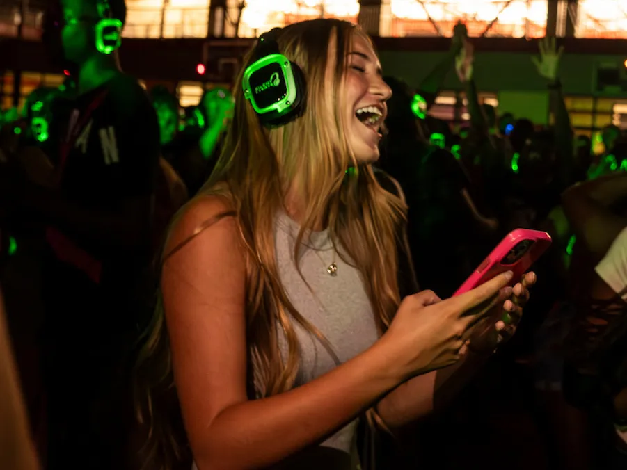 Student laughs with headphones at a silent disco party on campus.