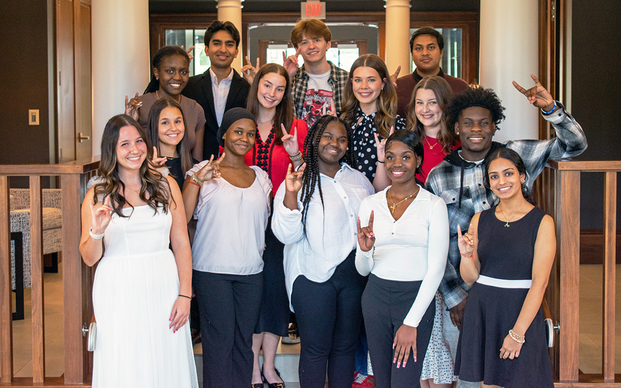 A group of Arkansas State University students pose together indoors, smiling and making the Wolves Up hand sign, representing school spirit and community.