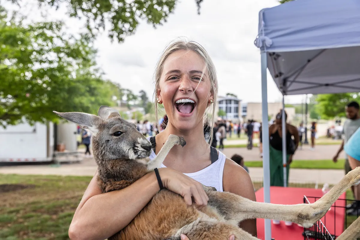 Smiling student holds a kangaroo during a fun outdoor campus event.