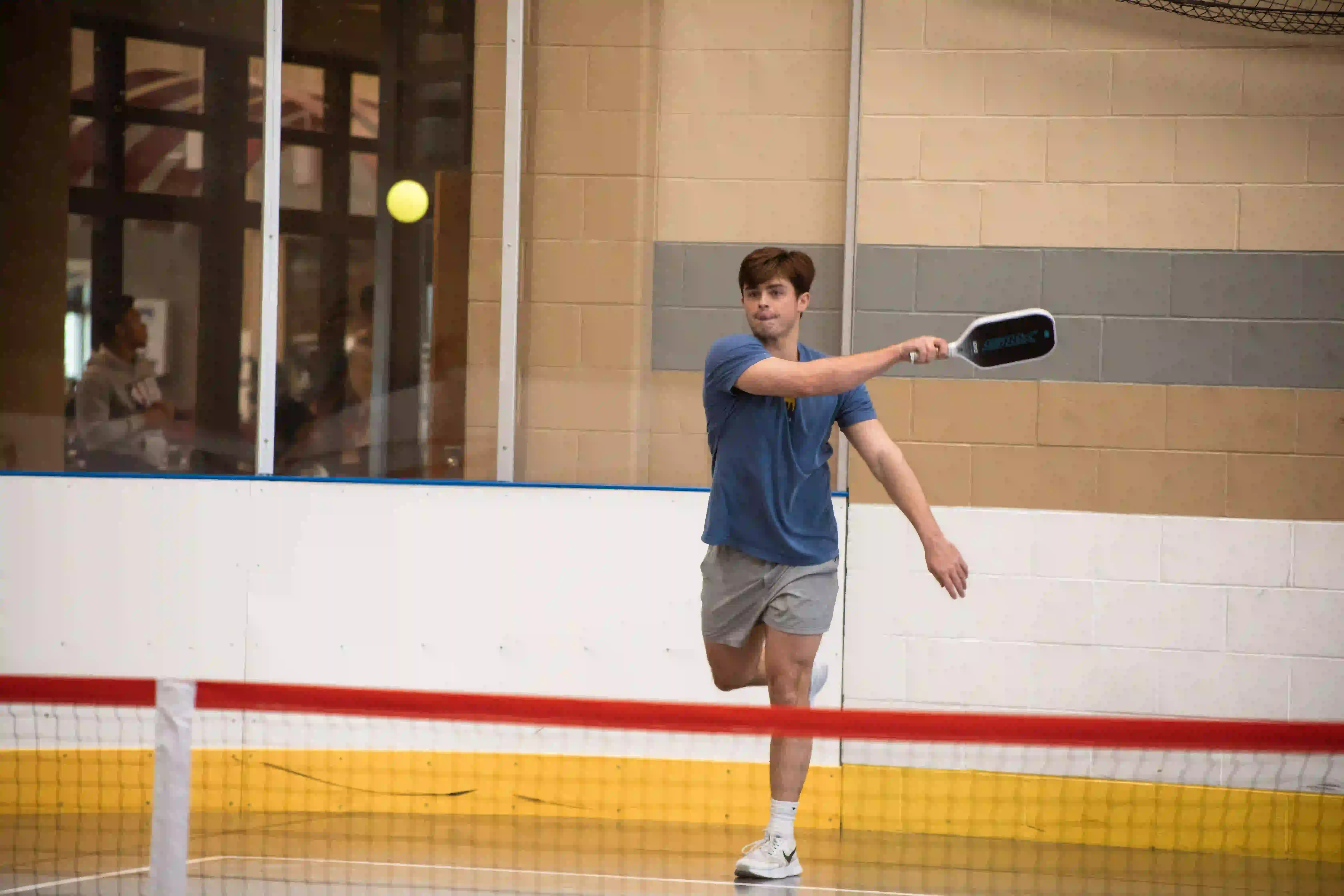 Student swinging paddle while playing pickleball in gym.