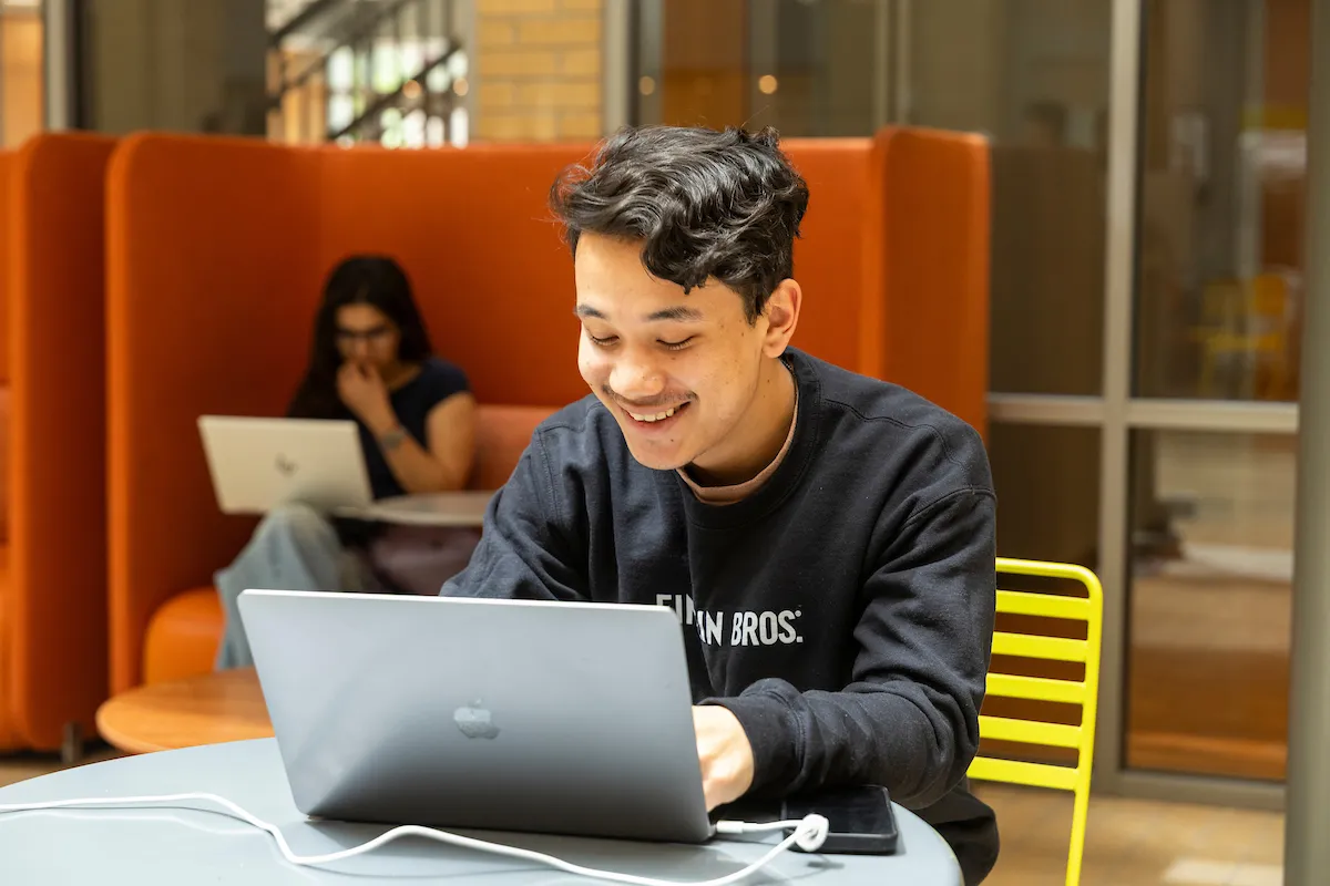 A student works on a laptop in the Humanities and Social Sciences Building atrium.
