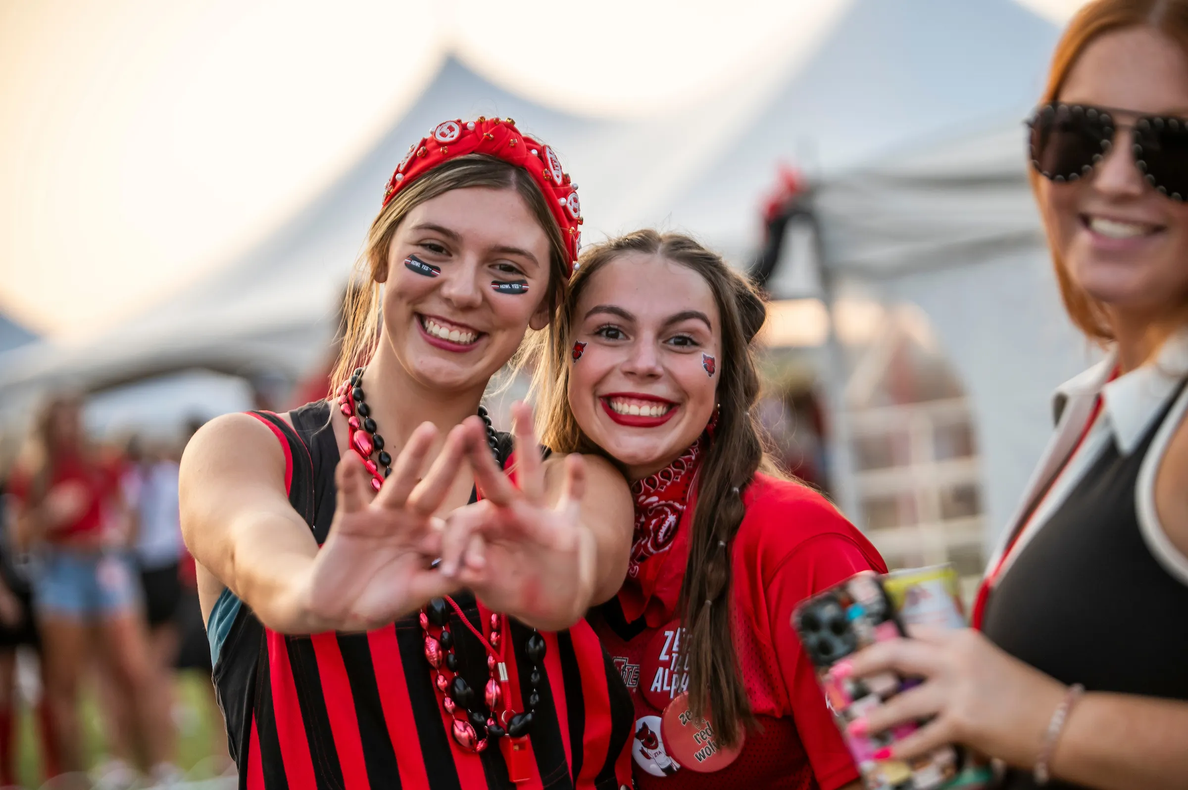 Two students in red and black show spirit while celebrating at a tailgate event.