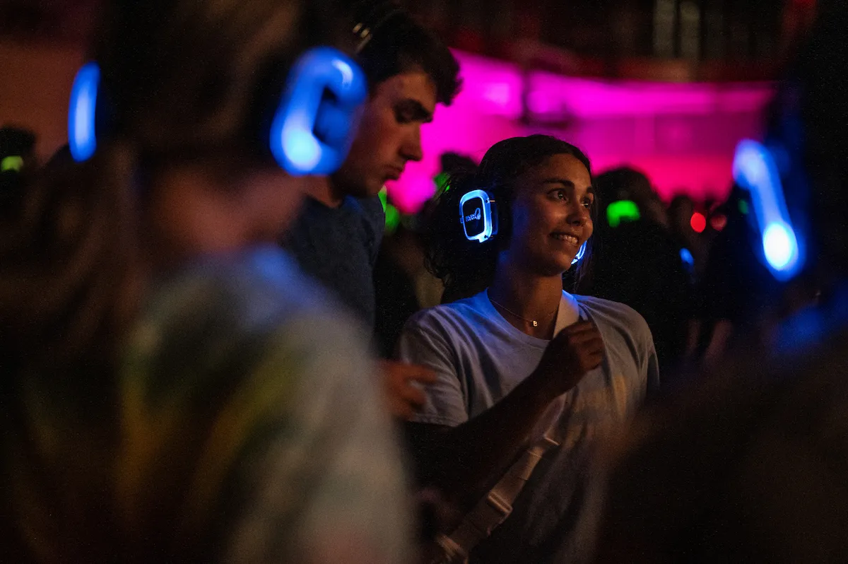 Students wearing glowing headphones dance at a silent disco on campus.