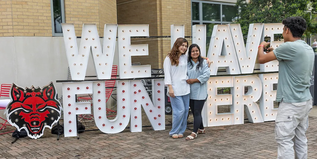 Students pose by a large “We Have Fun Here” sign with Red Wolves logo.