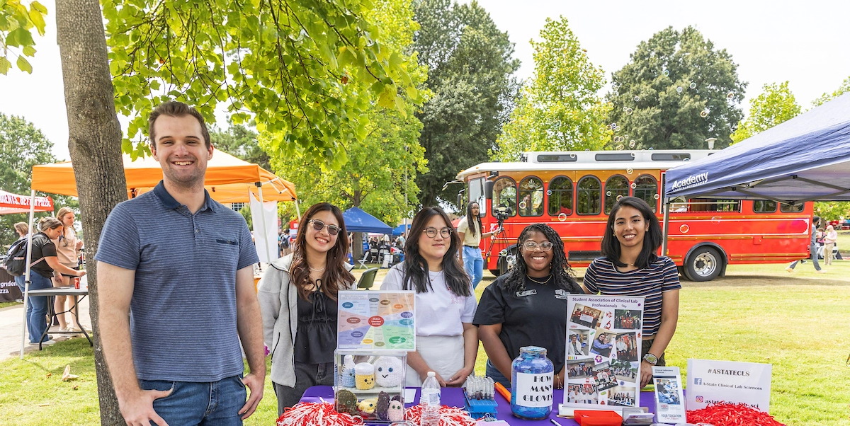 Students standing at table promoting their student organization at the annual Community Fair.