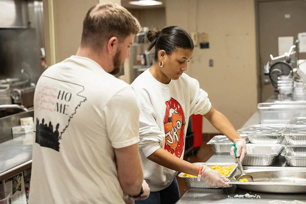 Students volunteer by preparing and serving food in a kitchen.