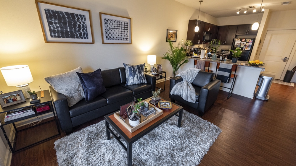 Living room with sofa and armchair next to kitchen bar with stools and pendant lighting.