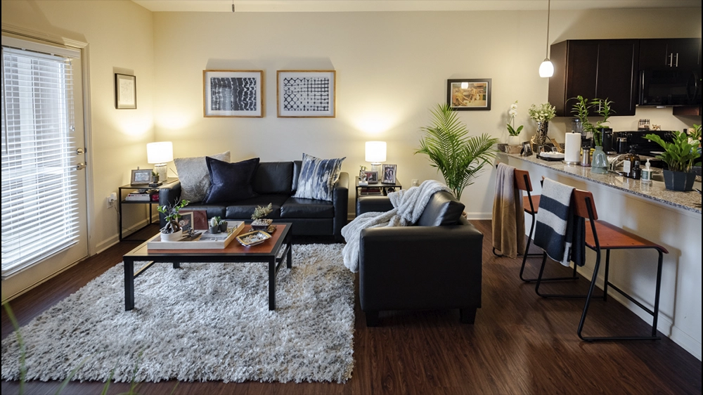 View of living room from bedroom doorway, showing seating area, coffee table, and kitchen bar with stools.
