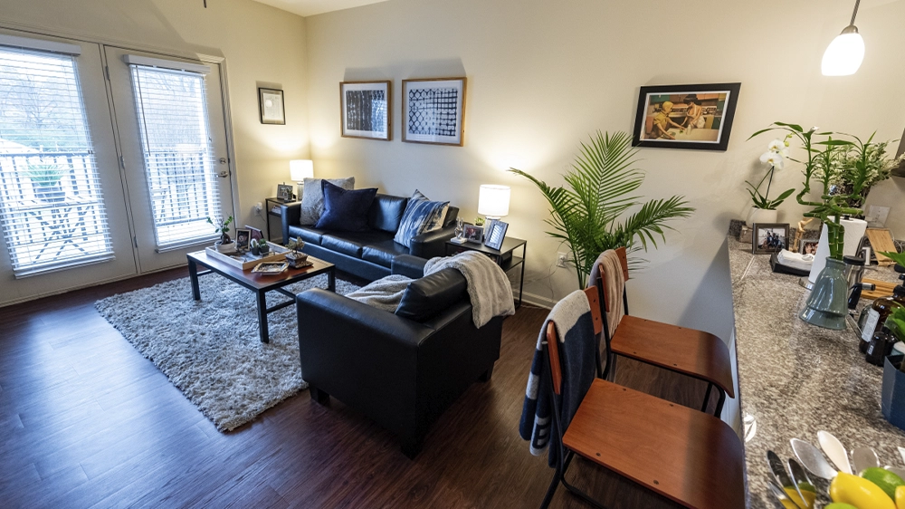 Living room with black leather sofa, coffee table, area rug, and glass doors leading to balcony.