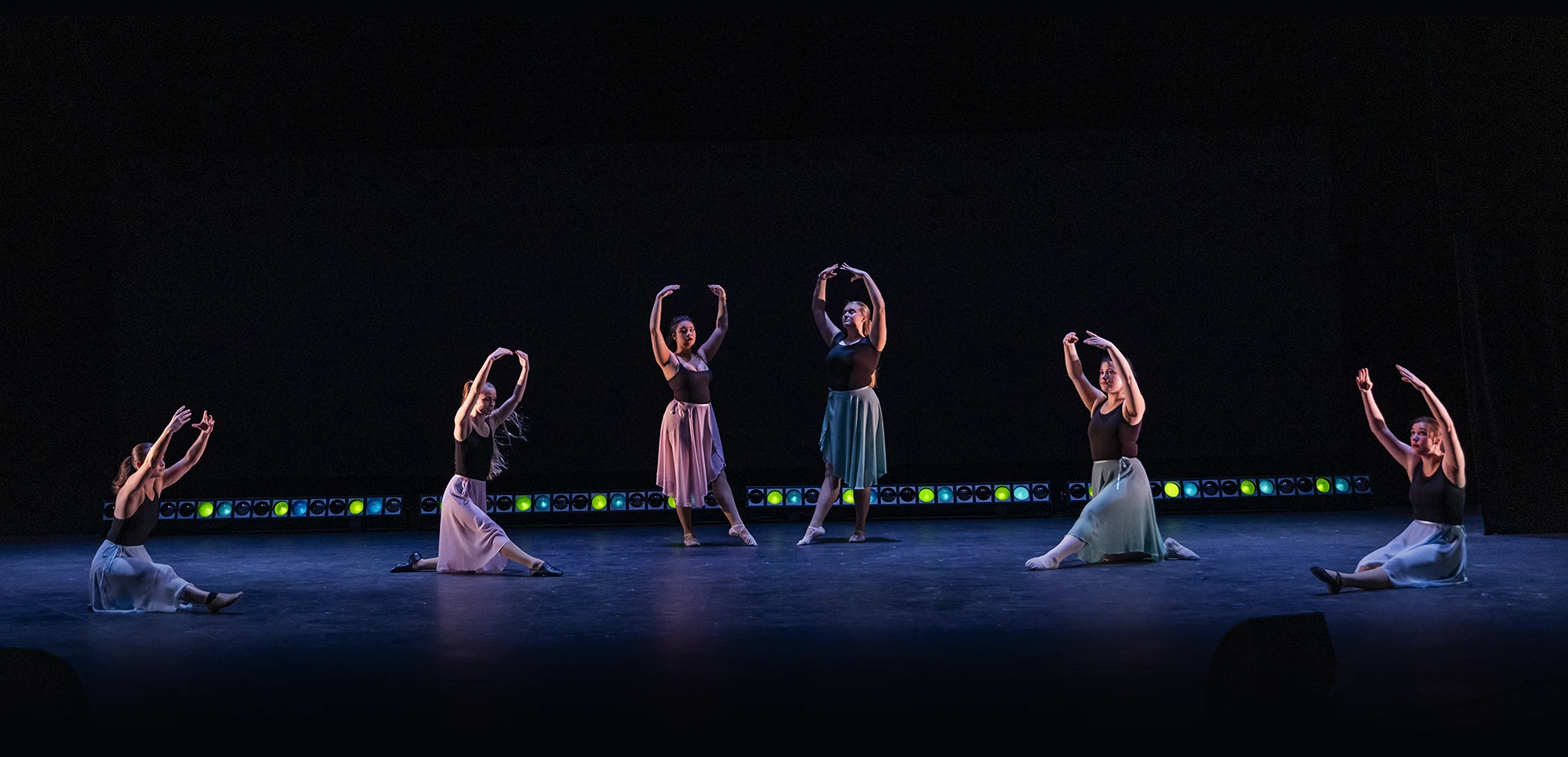 Dancers sit on stage, moving in sync.