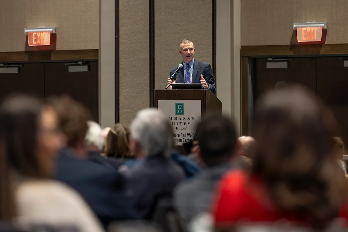 Man in suit speaks at a podium to an audience during a business conference.