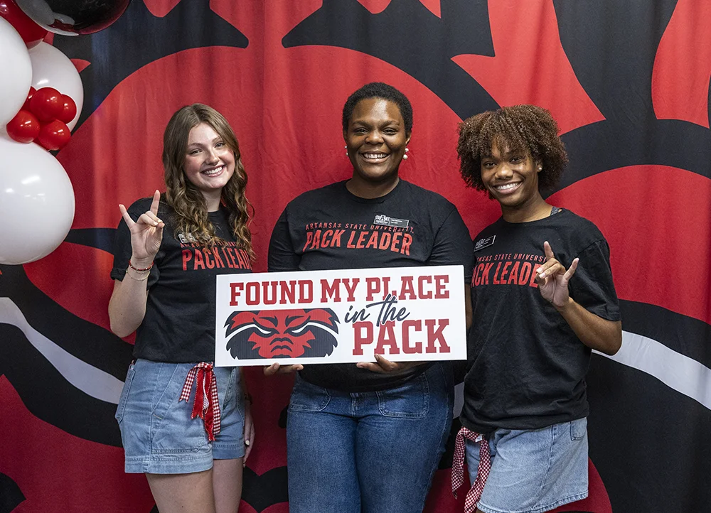 Three students posing with a sign that says "I found my place in the Pack".