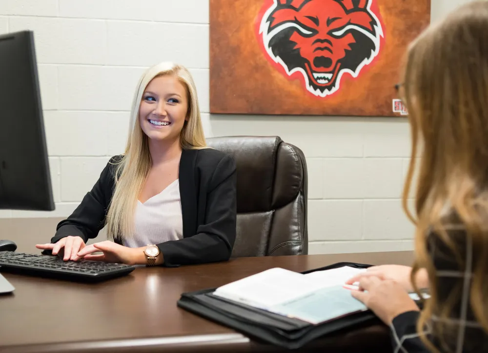 A girl smiling at a desk with a Red Wolves painting behind her.