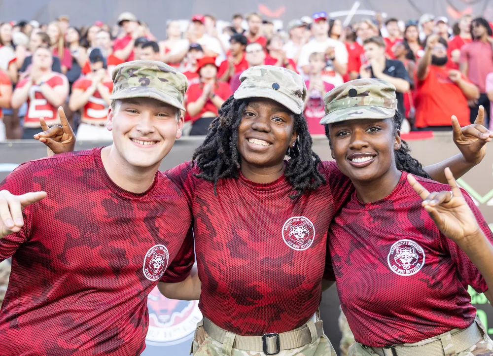 ROTC students in A-State military uniforms doing Wolves Up.