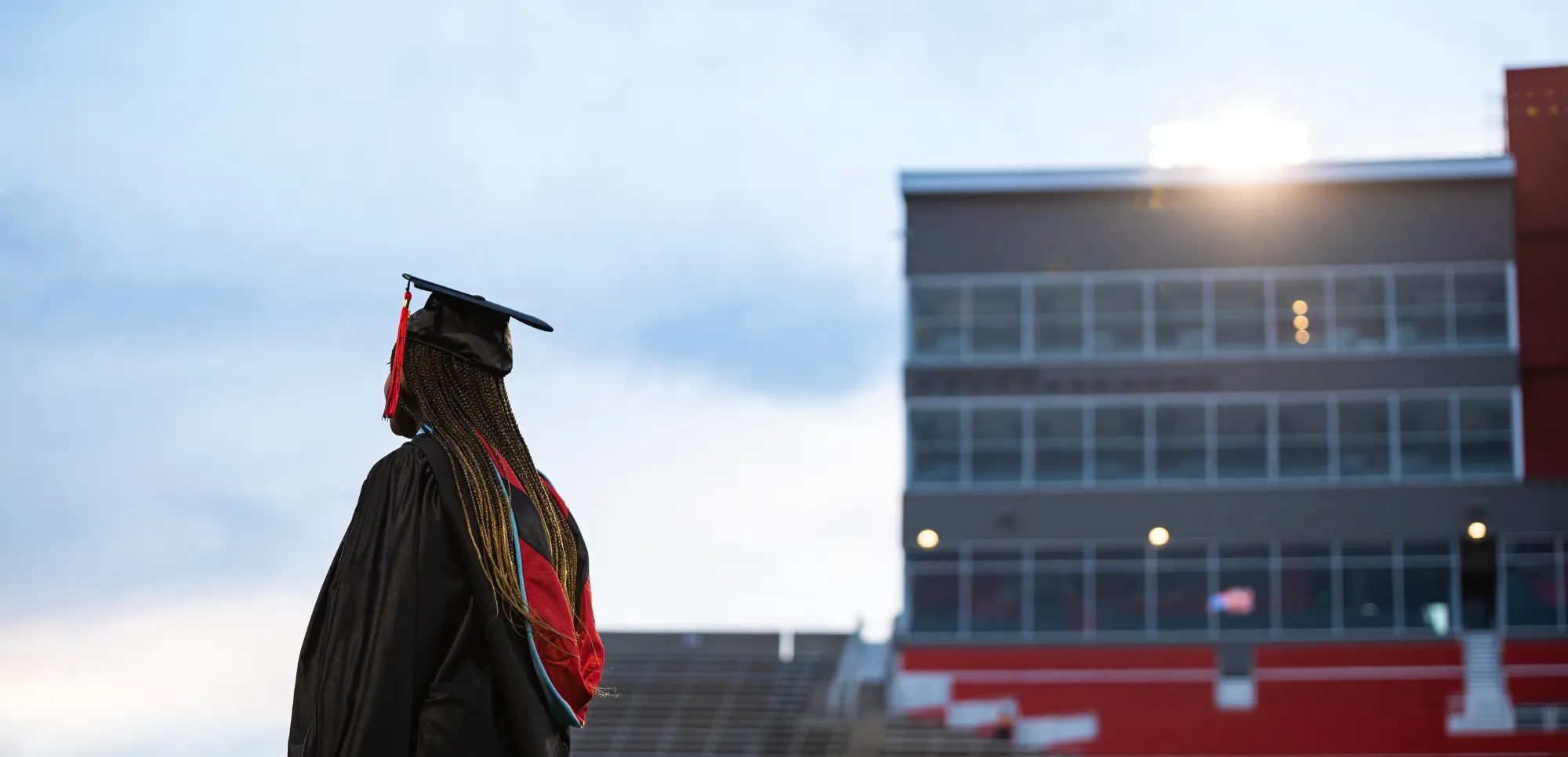 Student standing outside on the football field with a doctorate graduate sash and cap and gown.